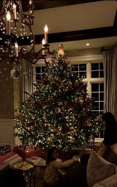 a woman and child sitting in front of a christmas tree