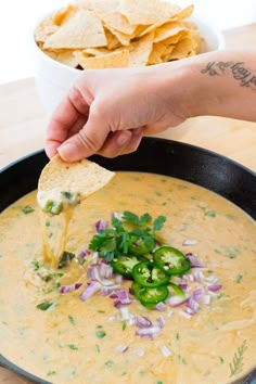 a person dipping tortilla chips into a bowl of quesadilla soup