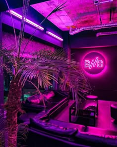 a purple lit room with couches and a palm tree in the corner, next to a neon sign that reads bwb