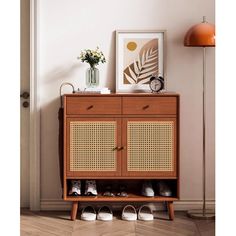 a wooden cabinet with shoes on it in front of a white wall and an orange lamp