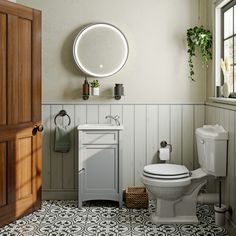 a white toilet sitting next to a sink in a bathroom under a mirror and potted plant