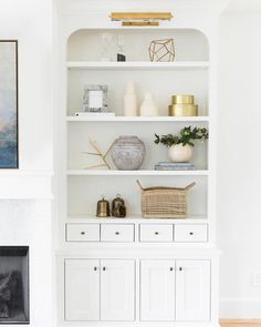 a living room with white bookcases filled with books and vases on top of them