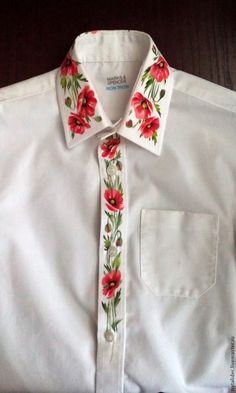 a white shirt with red flowers and green leaves on the collar is sitting on a table