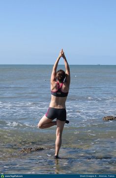 a woman doing yoga on the beach in front of the ocean with her hands up