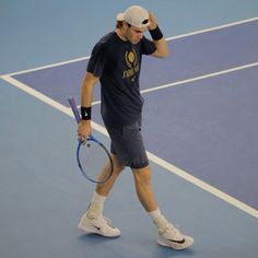 a man walking across a tennis court holding a racquet in his left hand