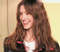 a woman with long hair smiling and wearing a black leather jacket over a white t - shirt