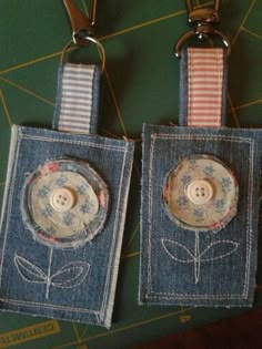 two blue jean purses with flowers and buttons attached to the handles, hanging on a green board