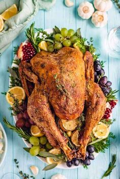 a roasted turkey on a platter with grapes, lemons and herbs