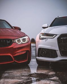 two cars parked side by side on a wet parking lot, one is red and the other is white