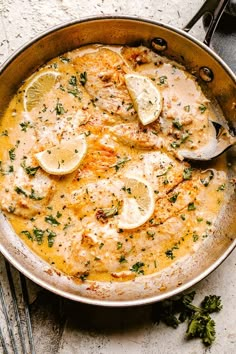 a skillet filled with chicken and lemons on top of a table next to utensils