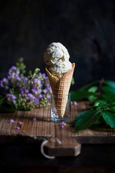 an ice cream cone sitting on top of a wooden table next to some purple flowers