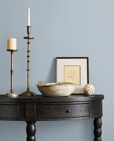 a wooden table topped with a bowl and two candles next to a framed photograph on the wall