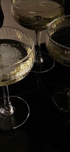 two martini glasses filled with white wine on top of a black counter