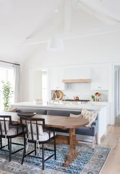 a kitchen with white walls and wooden flooring has an island table surrounded by chairs