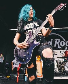 a woman with blue hair playing an electric guitar