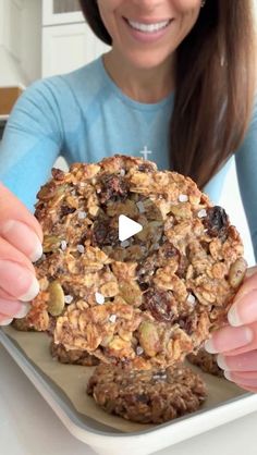 a woman holding up a cookie with nuts and raisins on it