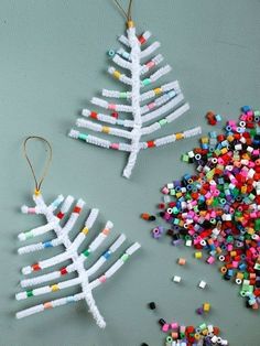 two christmas tree ornaments made out of plastic tubes and beads on a gray surface with other crafting supplies