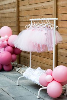 some pink and white balloons are hanging from a clothes rack with tulle skirts on it