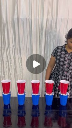 a woman standing in front of a table filled with red and blue cups on top of it