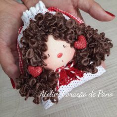 a hand holding a small doll with brown hair and red bows on it's head