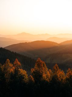 the sun is setting over mountains with trees in the foreground and hills in the background