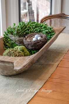 a wooden bowl filled with green plants and birds'nests on top of a table