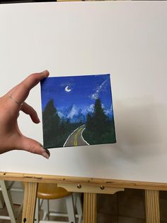 a hand holding up a small card with a road going to the moon on it