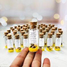 a hand holding a tiny bottle filled with yellow liquid next to small bottles full of them