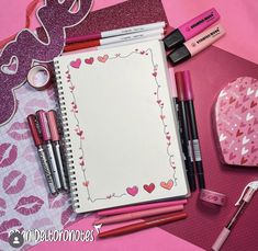 notebooks, pens, and other items are arranged on a pink surface with hearts