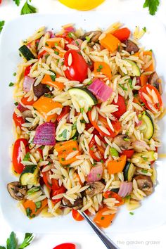 a white plate topped with pasta salad next to tomatoes and cucumbers on a table