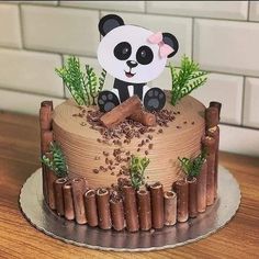 a cake decorated with a panda bear and bamboo sticks on a wooden table next to a white brick wall