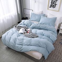 an unmade bed with blue sheets and pillows on the floor in front of a window