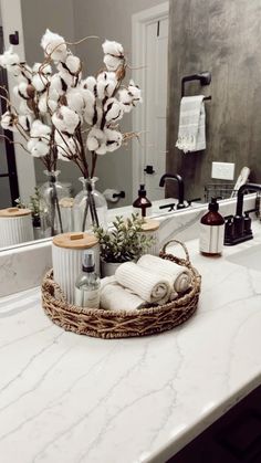 a bathroom counter topped with a basket filled with cotton flowers and other items next to a mirror