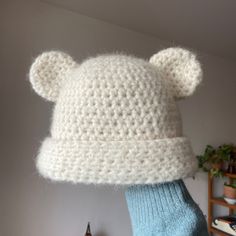 a white knitted bear hat on top of someone's blue handmade mitt