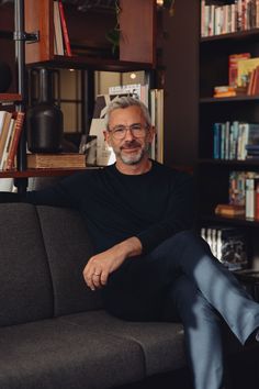 a man sitting on top of a couch in front of a book shelf filled with books