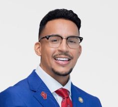 a man in a blue suit and red tie smiles at the camera while wearing glasses