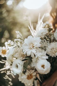 a woman holding a bouquet of white flowers in her hands with sunlight streaming through the background