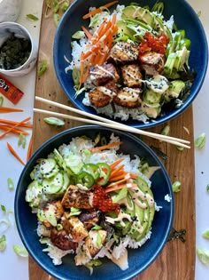 two blue bowls filled with food on top of a wooden cutting board next to chopsticks