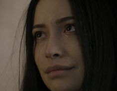 a close up of a woman's face with tears on her eyes and dark hair