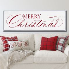 a white couch with red and black pillows on it in front of a merry christmas sign