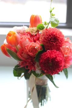 a vase filled with red and orange flowers on top of a table next to a window