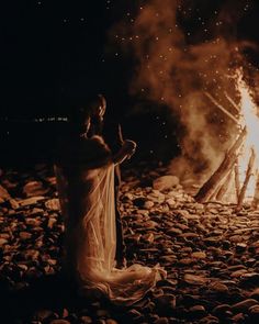 a man and woman standing in front of a campfire with their hands up to the sky