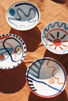 three colorful plates sitting on top of a brown cloth covered ground with circles and shapes painted on them