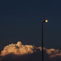 an airplane is flying in the sky with clouds behind it and a street light at night