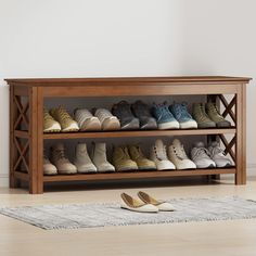 a wooden shoe rack filled with pairs of shoes next to a white rug on the floor