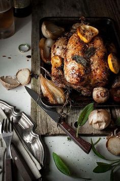 a roasting pan filled with chicken, mushrooms and garlic on a wooden cutting board