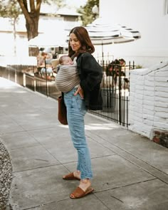 a woman standing on the sidewalk holding a baby in her arms and looking at something