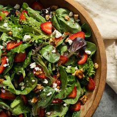 a salad with strawberries and feta cheese in a wooden bowl on a table