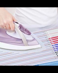 a person ironing fabric with an electric iron on top of papers and colored pencils