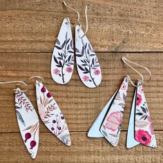 four pieces of paper with floral designs hanging from hooks on a wooden surface, one is white and the other has pink flowers